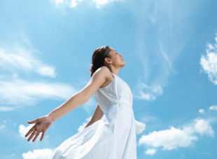 Image shows a woman in a white dress against a blue sky with clouds taking a deep breath